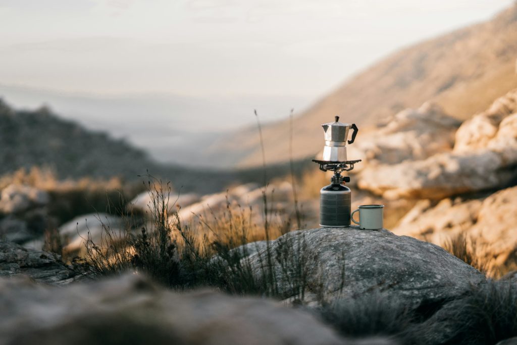Coffee brewing on a portable stove amidst mountains, capturing the essence of outdoor adventure.