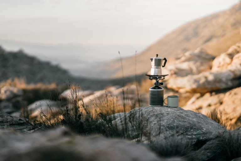 Coffee brewing on a portable stove amidst mountains, capturing the essence of outdoor adventure.